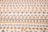 A fine beaded embroidery fabric, with a vertical stripe pattern made of tiny floral and starburst motifs in champagne-pink and pewter.