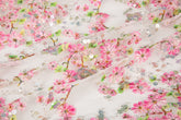 A fine embroidery fabric on white tulle, with a pattern of pink cherry blossom branches and shimmering sequins.