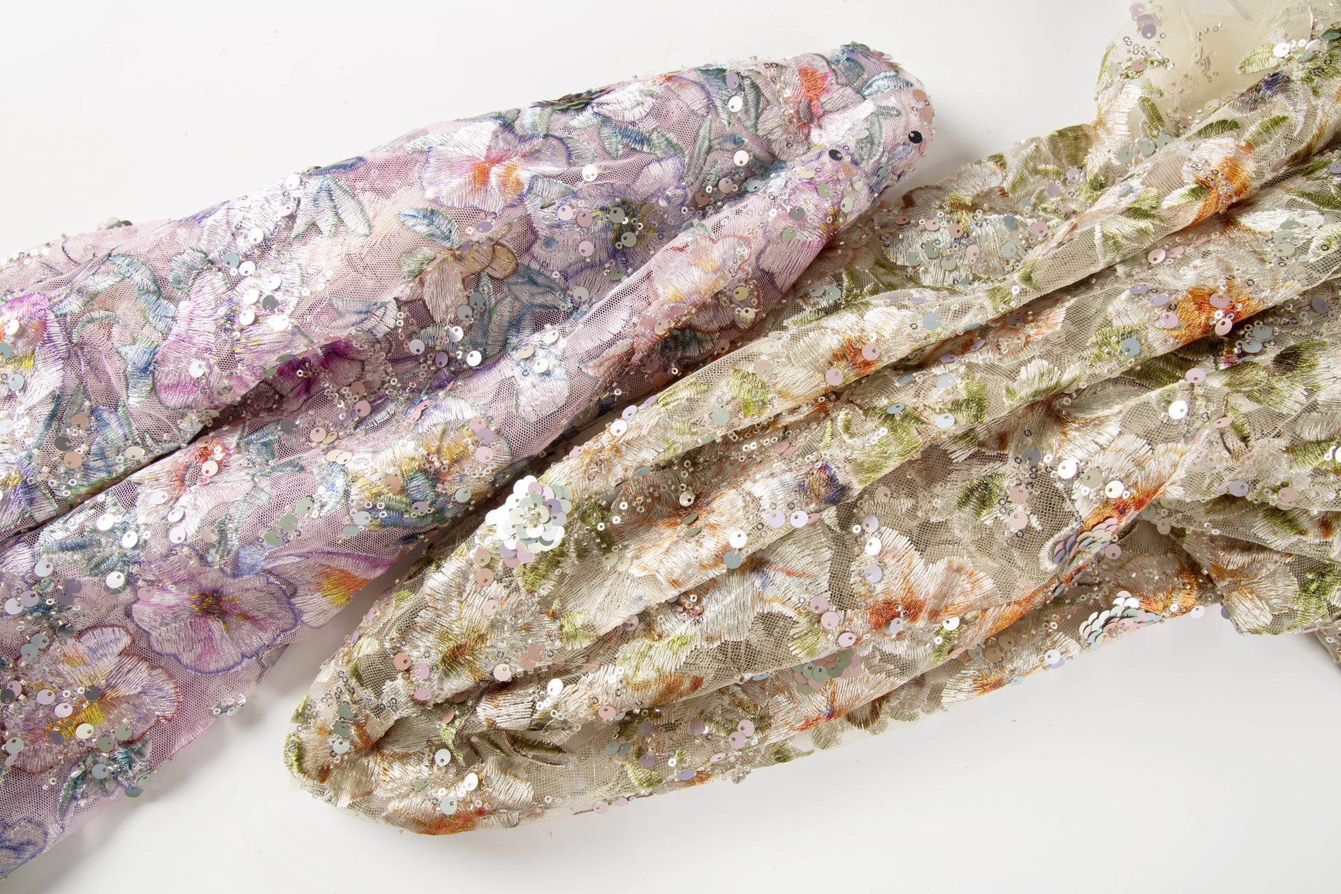 A multi-color floral embroidery fabric on a  lavender mesh base, with a pattern made of embroidery thread, sequins, and black beads.