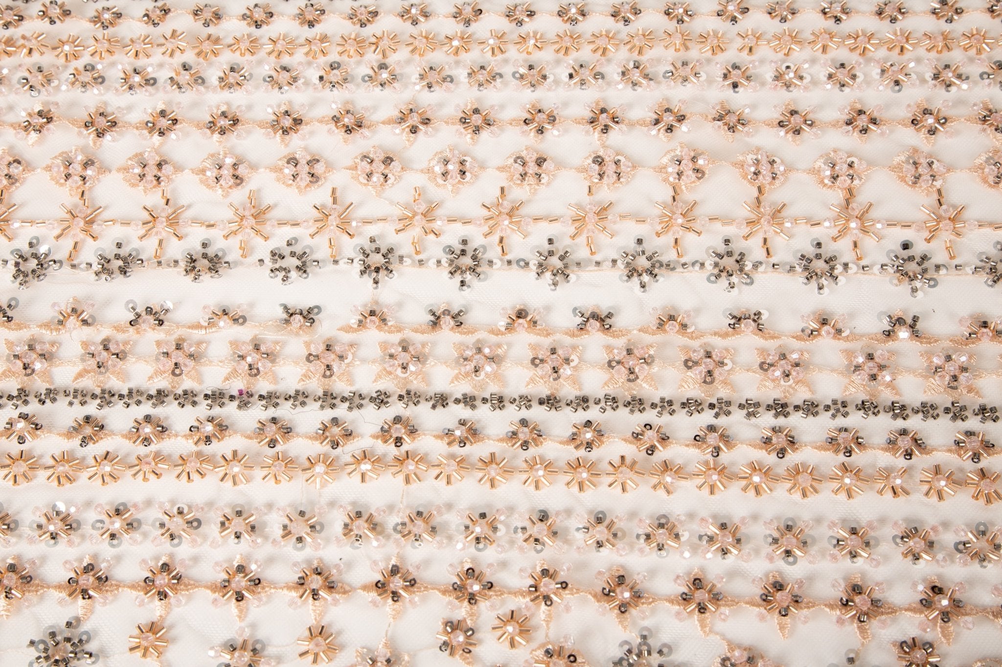A fine beaded embroidery fabric, with a vertical stripe pattern made of tiny floral and starburst motifs in champagne-pink and pewter.