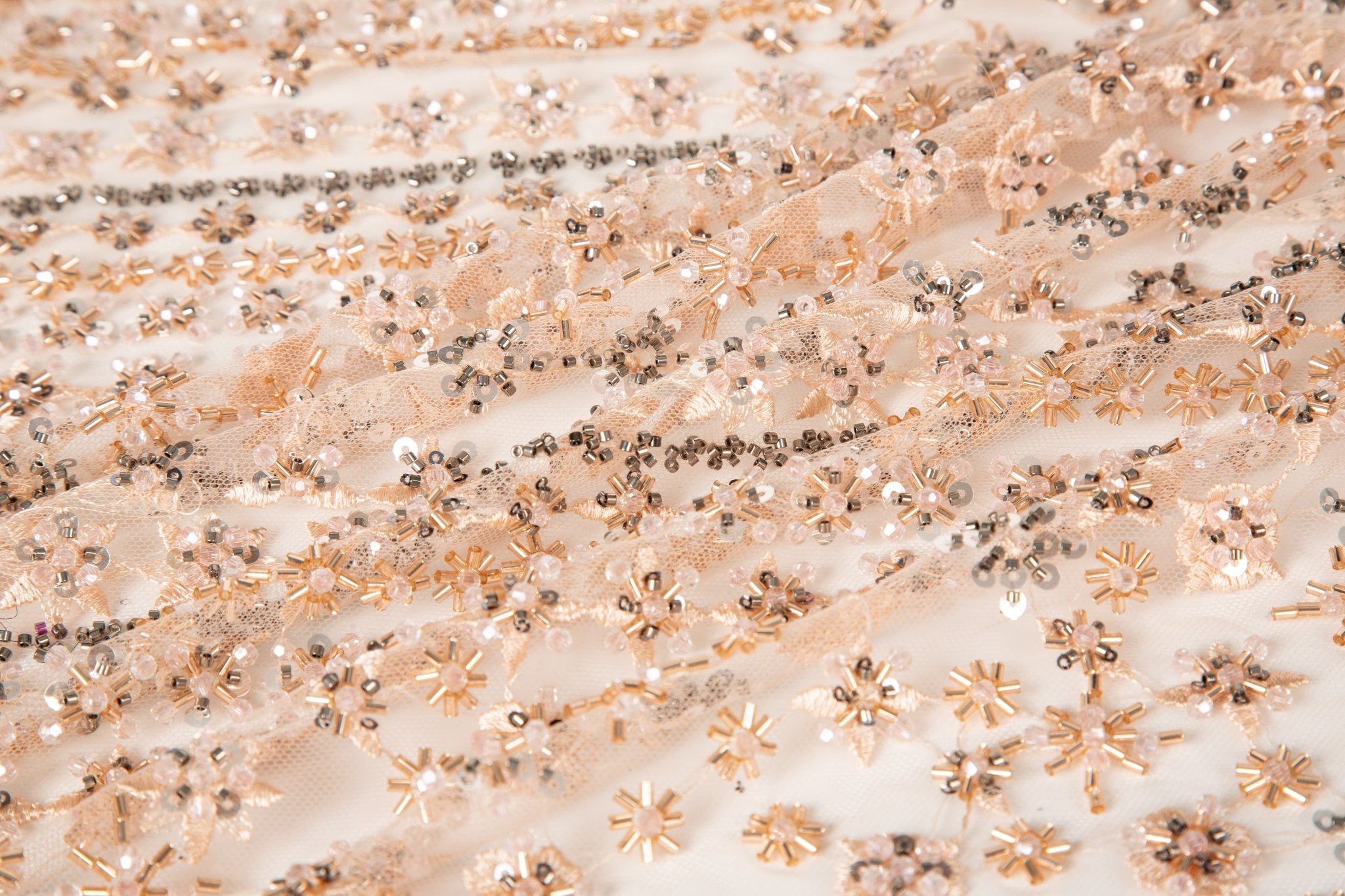 A fine beaded embroidery fabric, with a vertical stripe pattern made of tiny floral and starburst motifs in champagne-pink and pewter.