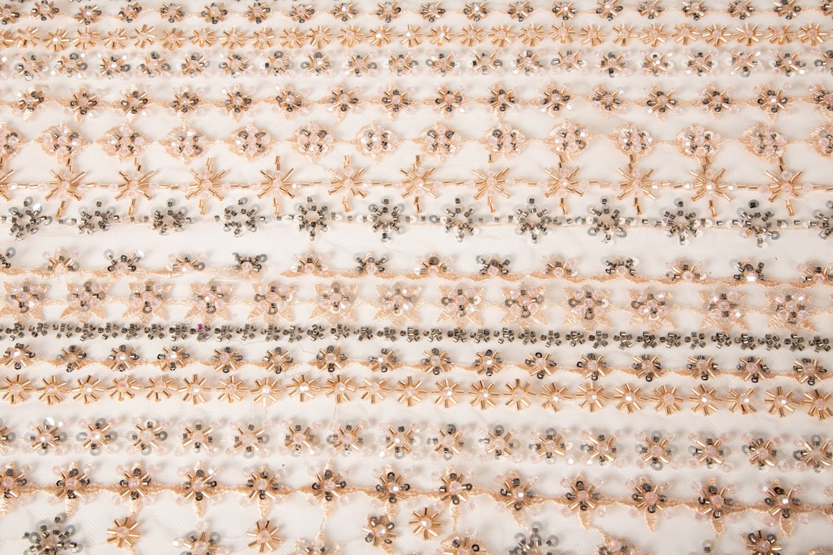 A fine beaded embroidery fabric, with a vertical stripe pattern made of tiny floral and starburst motifs in champagne-pink and pewter.