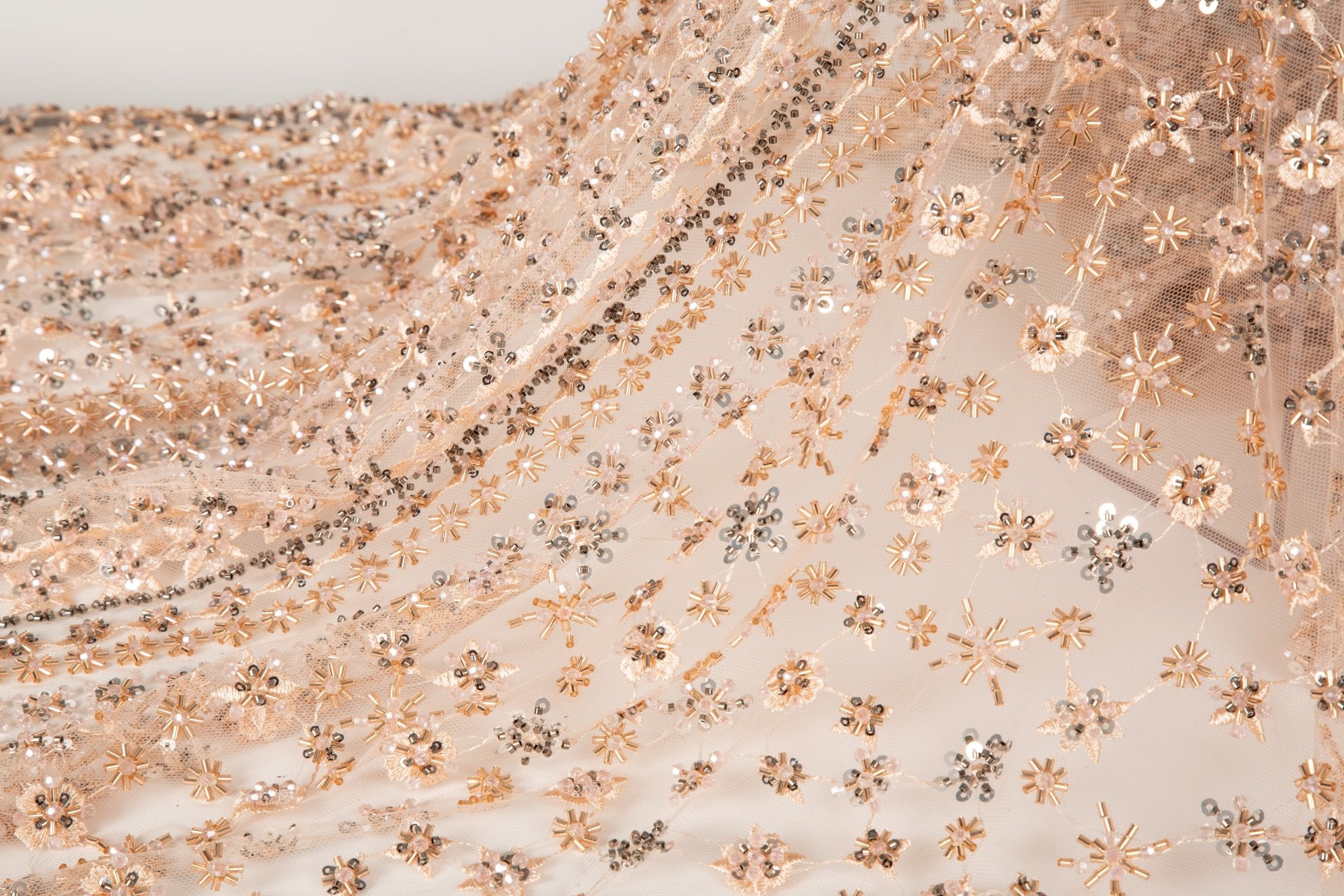 A fine beaded embroidery fabric, with a vertical stripe pattern made of tiny floral and starburst motifs in champagne-pink and pewter.
