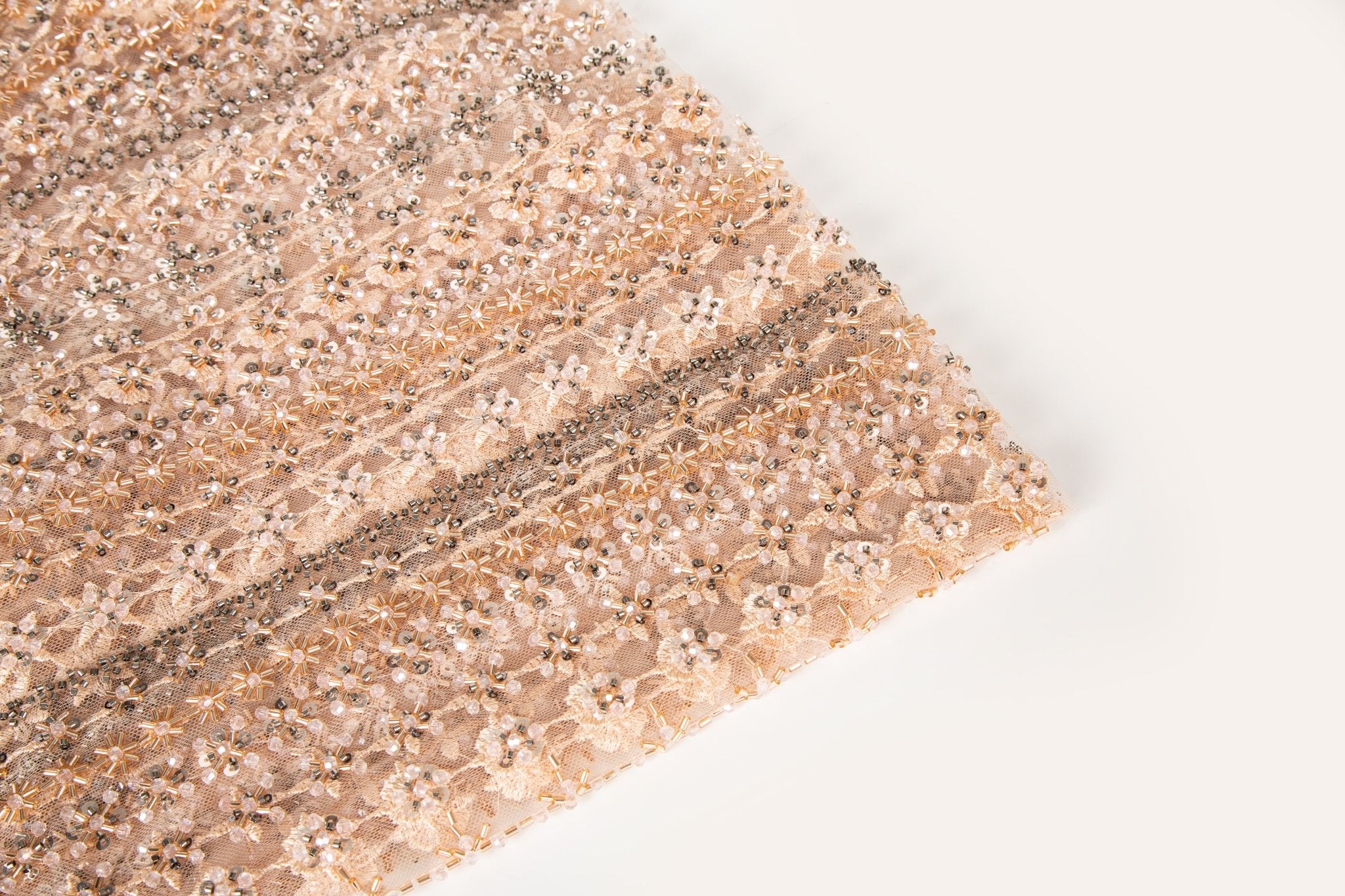 A fine beaded embroidery fabric, with a vertical stripe pattern made of tiny floral and starburst motifs in champagne-pink and pewter.