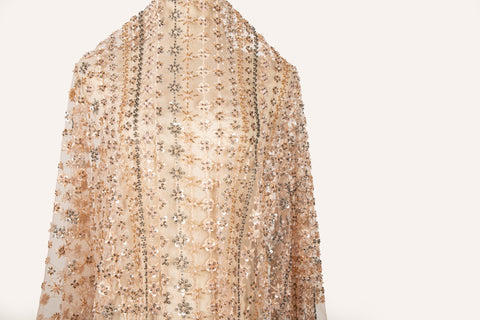 A fine beaded embroidery fabric, with a vertical stripe pattern made of tiny floral and starburst motifs in champagne-pink and pewter.