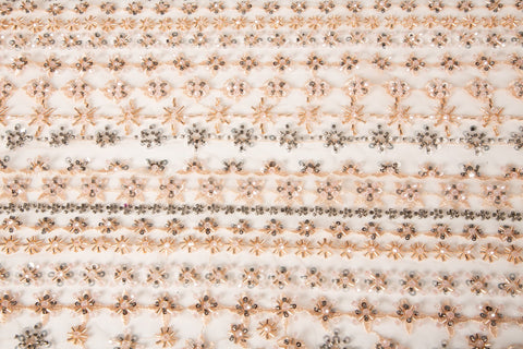 A fine beaded embroidery fabric, with a vertical stripe pattern made of tiny floral and starburst motifs in champagne-pink and pewter.