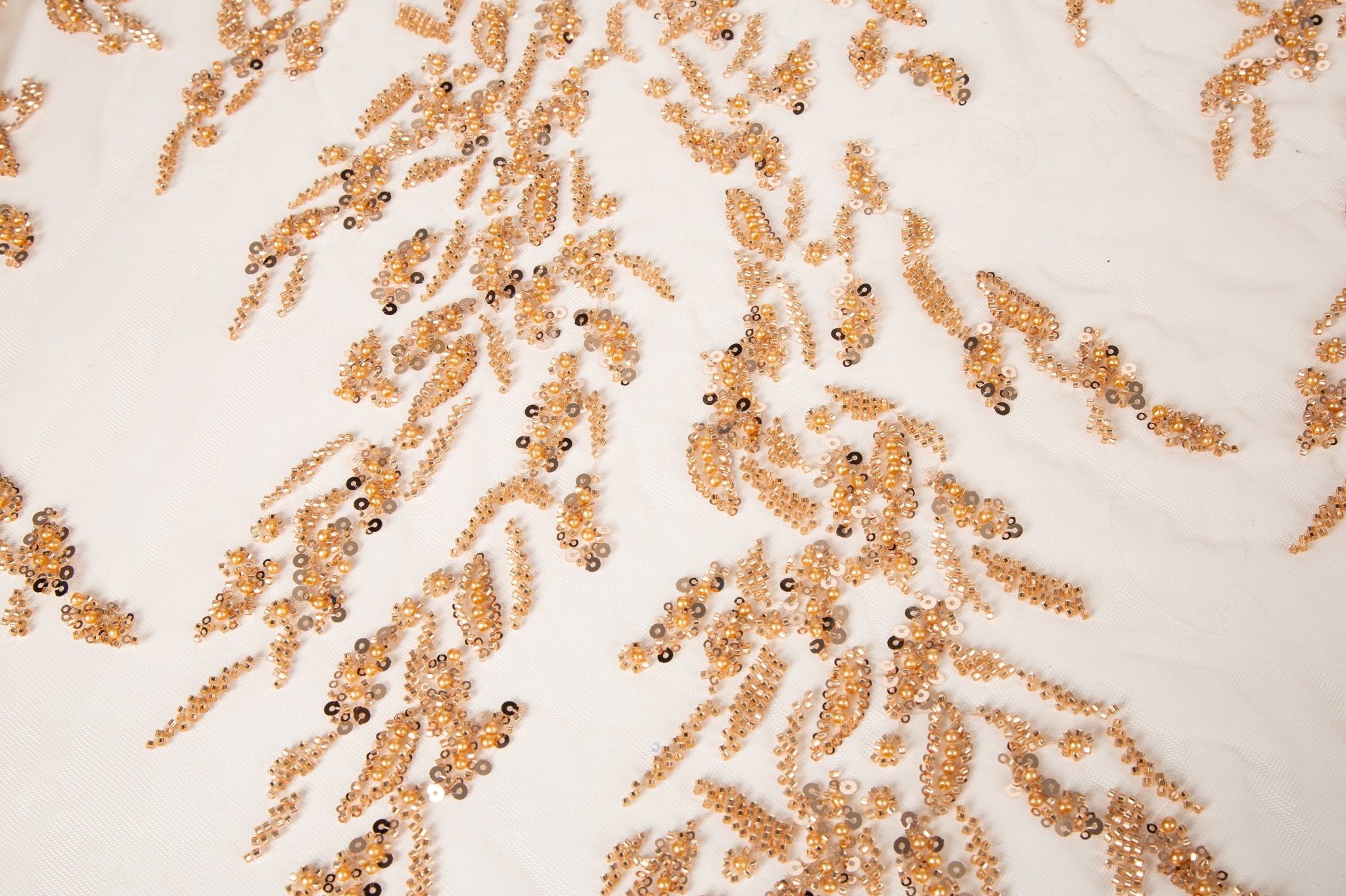 A hand-beaded embroidery fabric, with a pattern of fern-like leaves in a warm, copper-gold color palette.
