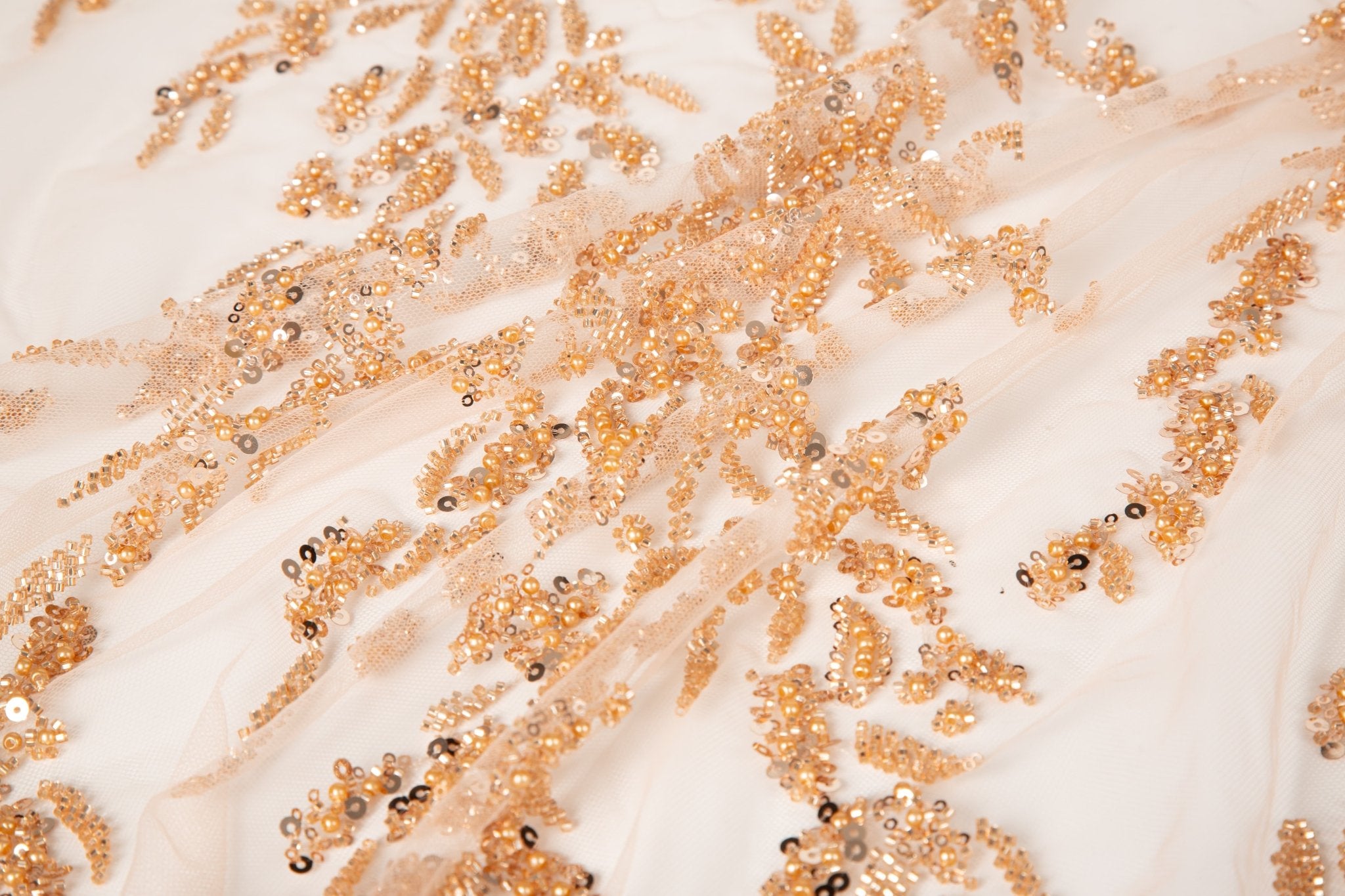 A hand-beaded embroidery fabric, with a pattern of fern-like leaves in a warm, copper-gold color palette.
