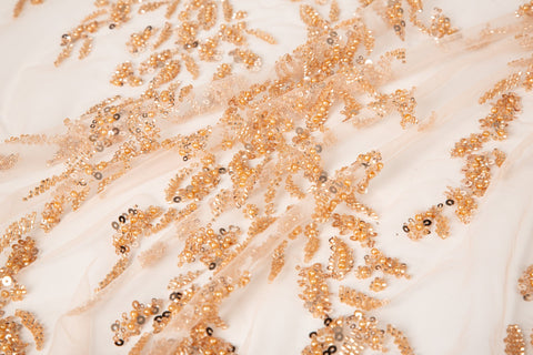 A hand-beaded embroidery fabric, with a pattern of fern-like leaves in a warm, copper-gold color palette.
