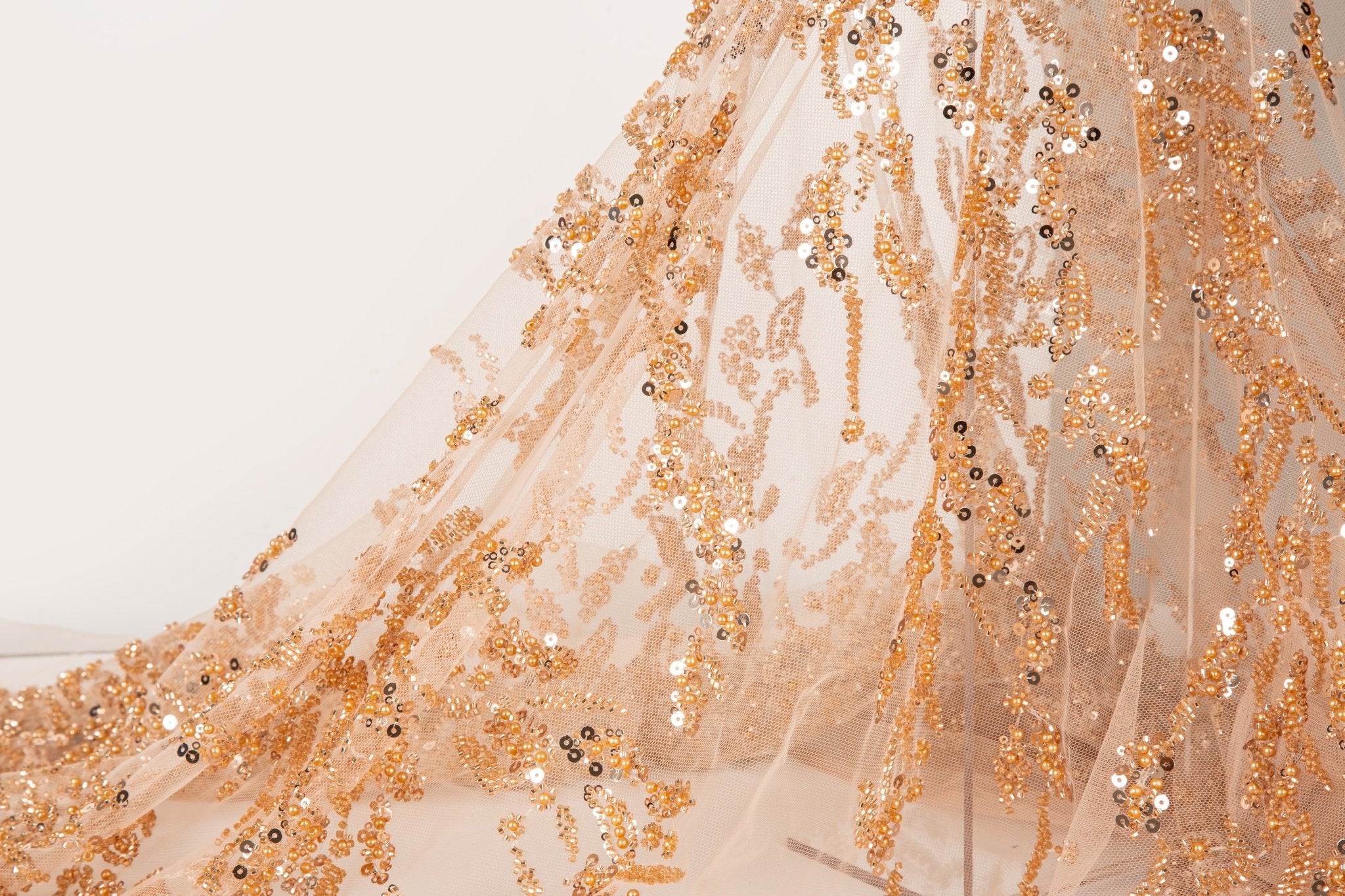 A hand-beaded embroidery fabric, with a pattern of fern-like leaves in a warm, copper-gold color palette.
