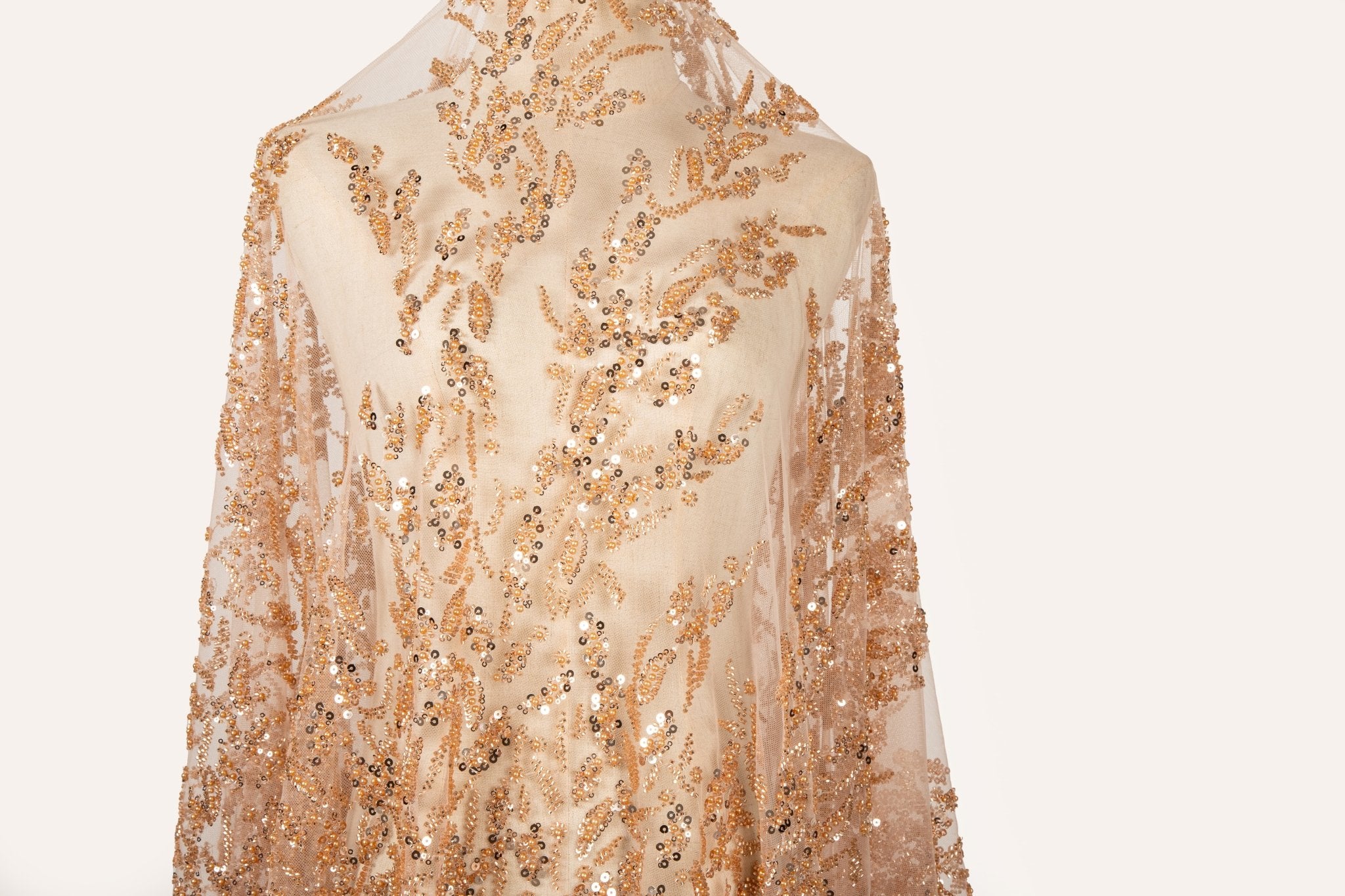 A hand-beaded embroidery fabric, with a pattern of fern-like leaves in a warm, copper-gold color palette.
