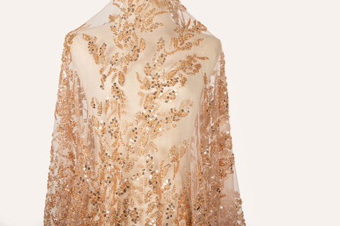 A hand-beaded embroidery fabric, with a pattern of fern-like leaves in a warm, copper-gold color palette.
