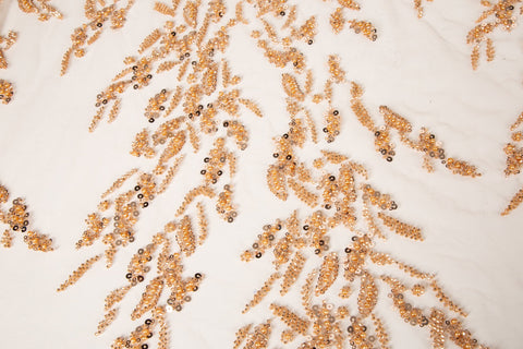 A hand-beaded embroidery fabric, with a pattern of fern-like leaves in a warm, copper-gold color palette.
