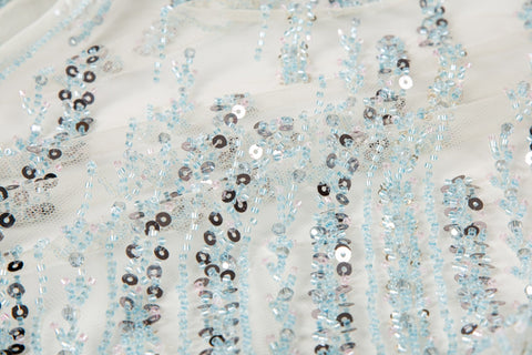 A fine beaded embroidery fabric, with a vertical dashed-line pattern resembling rain, in shades of ice blue and silver.