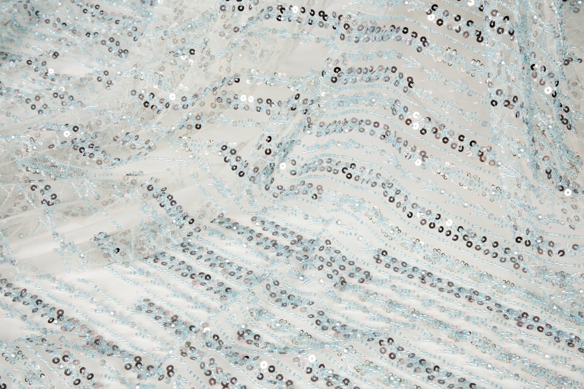 A fine beaded embroidery fabric, with a vertical dashed-line pattern resembling rain, in shades of ice blue and silver.