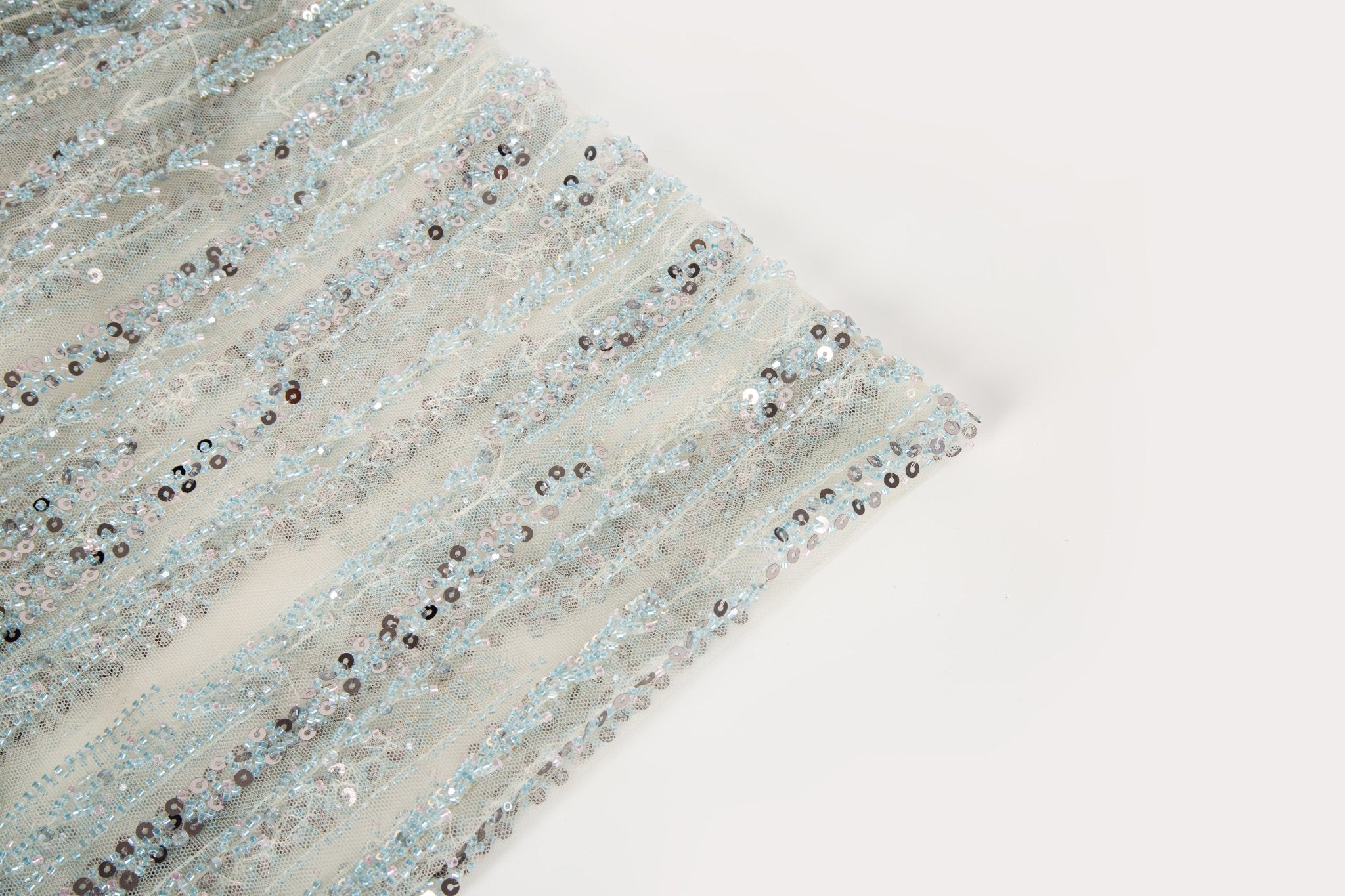 A fine beaded embroidery fabric, with a vertical dashed-line pattern resembling rain, in shades of ice blue and silver.