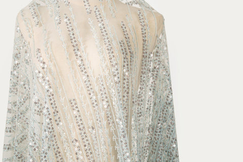 A fine beaded embroidery fabric, with a vertical dashed-line pattern resembling rain, in shades of ice blue and silver.