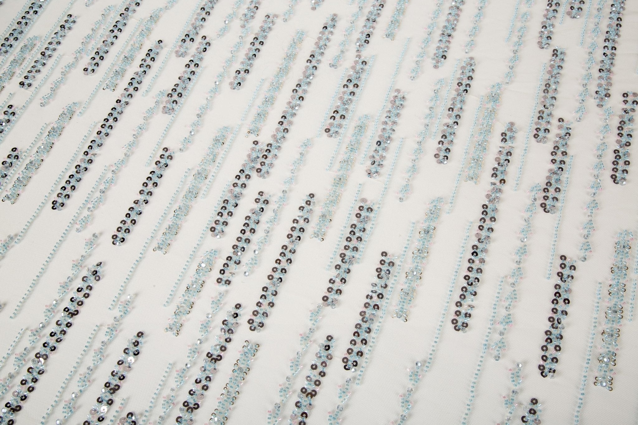A fine beaded embroidery fabric, with a vertical dashed-line pattern resembling rain, in shades of ice blue and silver.