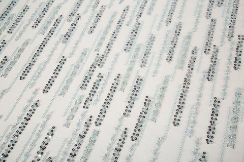 A fine beaded embroidery fabric, with a vertical dashed-line pattern resembling rain, in shades of ice blue and silver.