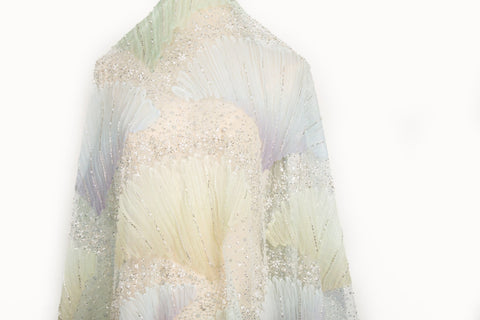 A 3D embroidery fabric with ribbon scallop motifs in a yellow, green, blue, and lilac gradient.
