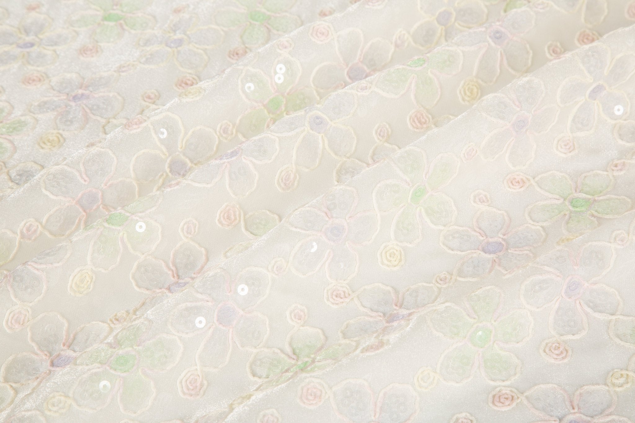White mesh fabric with small floral embroidery in lavender and light green threads, accented with iridescent sequins, draped softly.