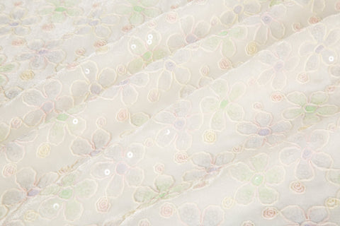 White mesh fabric with small floral embroidery in lavender and light green threads, accented with iridescent sequins, draped softly.