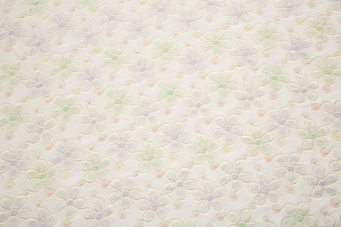 White mesh fabric with small floral embroidery in lavender and light green threads, accented with iridescent sequins, draped softly.