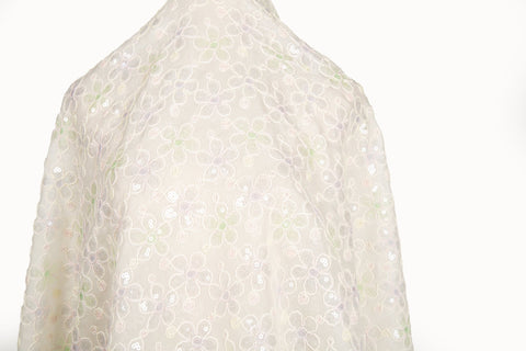 White mesh fabric with small floral embroidery in lavender and light green threads, accented with iridescent sequins, draped softly.