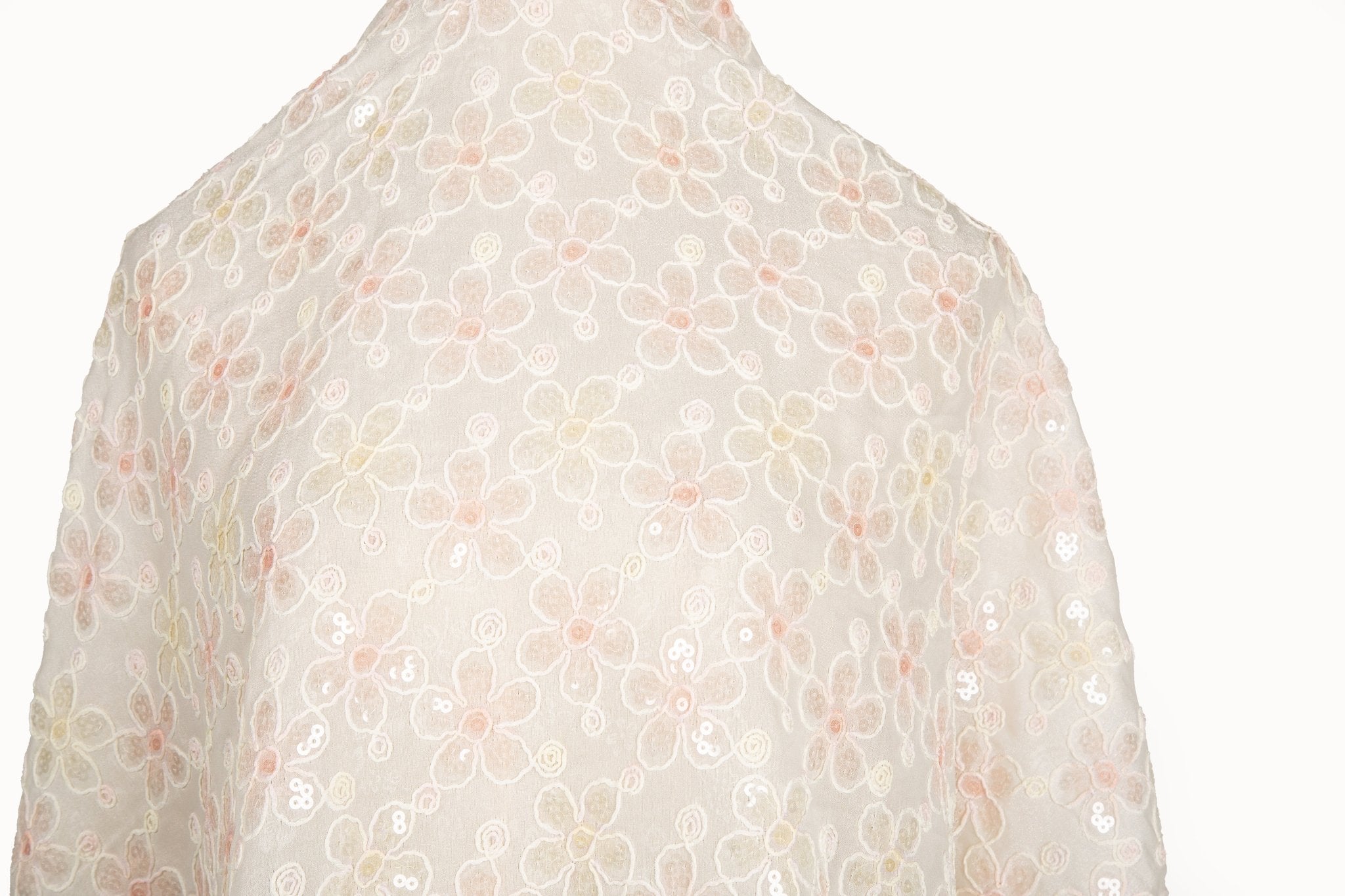 White mesh fabric with small floral embroidery in pale pink and daffodil yellow threads, accented with iridescent sequins, draped softly.
