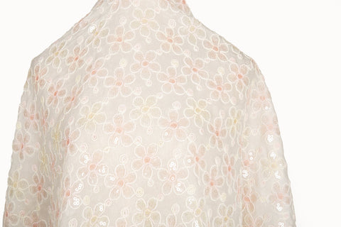 White mesh fabric with small floral embroidery in pale pink and daffodil yellow threads, accented with iridescent sequins, draped softly.