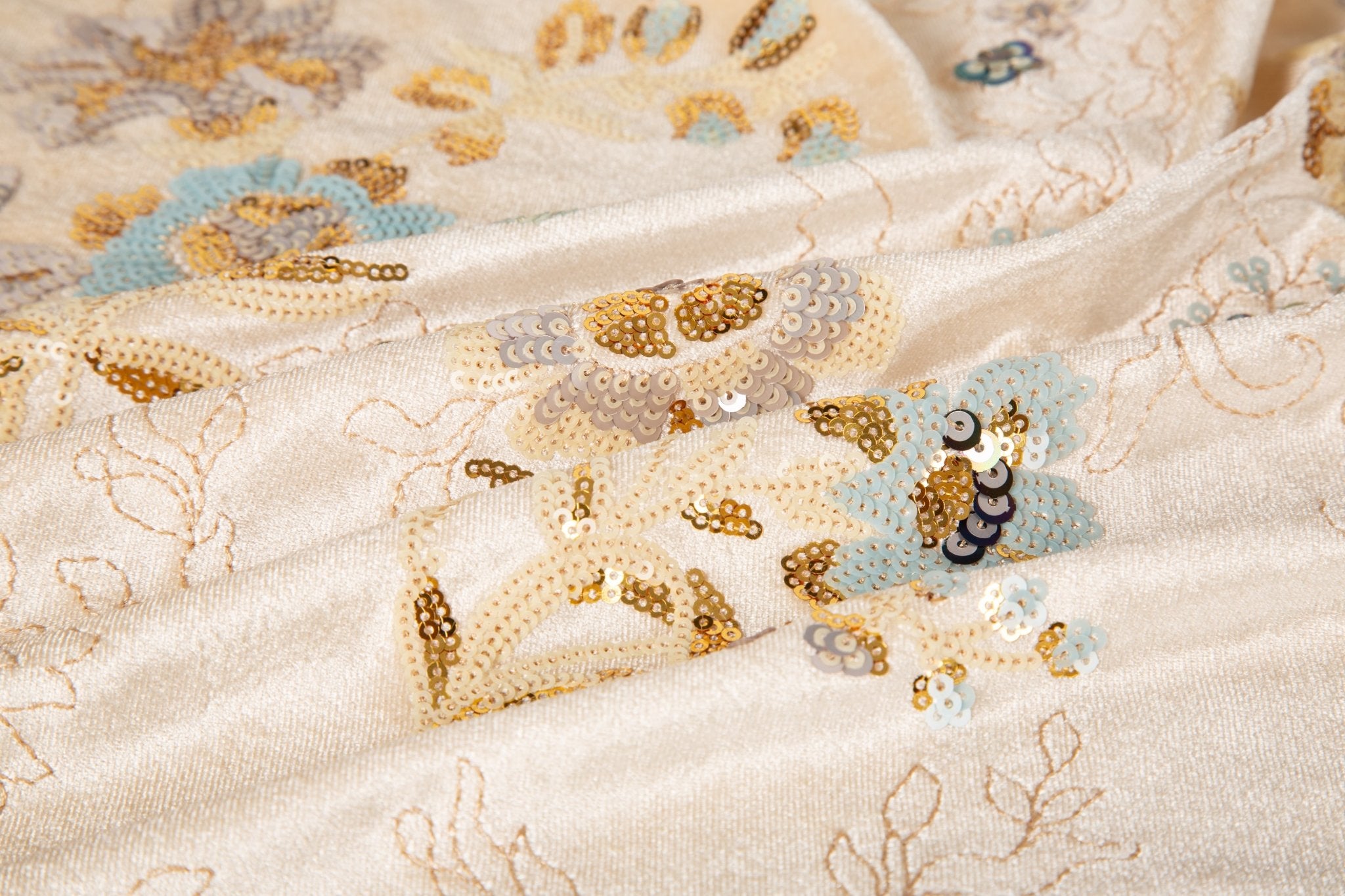 A sequin floral embroidery fabric on a cream velvet base, with blue and gold motifs.
