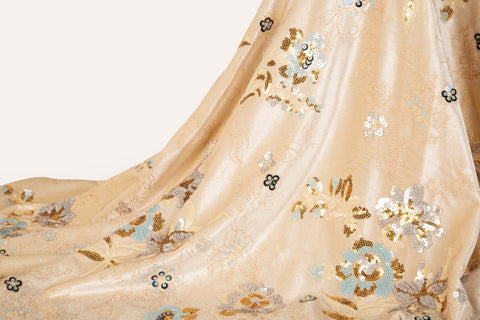 A sequin floral embroidery fabric on a cream velvet base, with blue and gold motifs.
