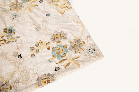 A sequin floral embroidery fabric on a cream velvet base, with blue and gold motifs.
