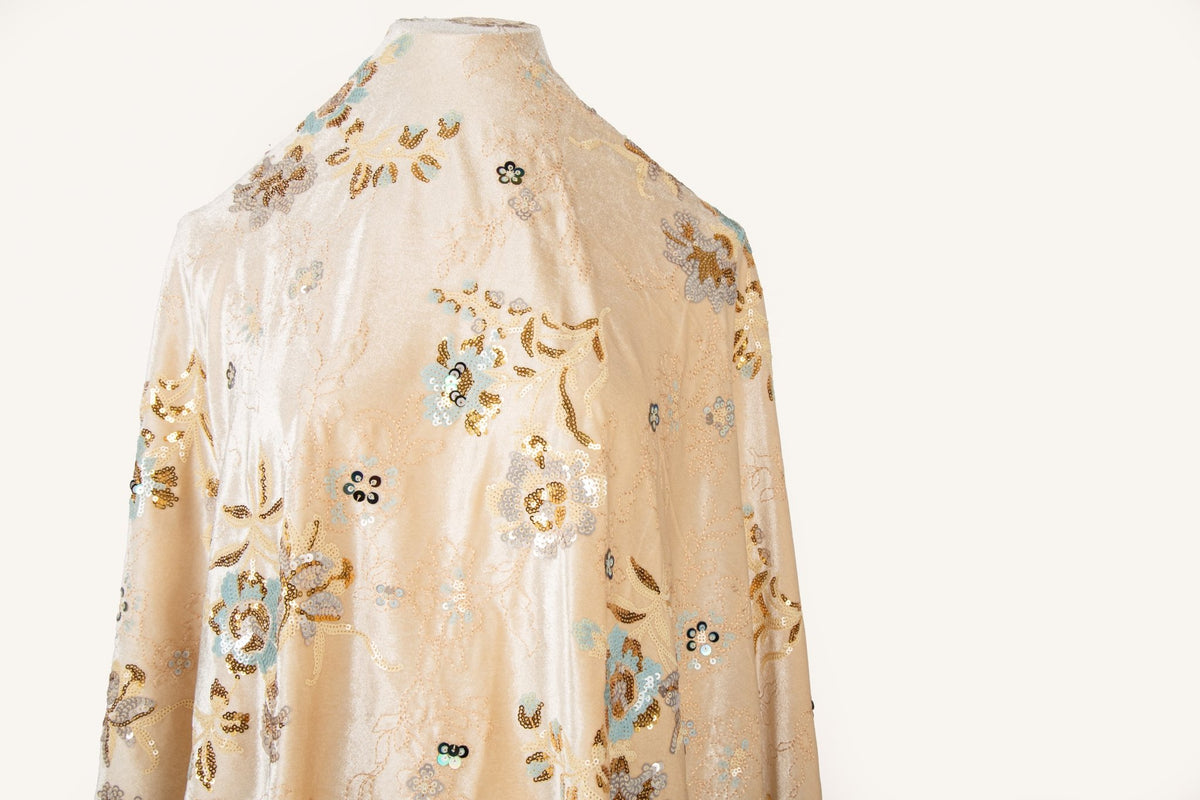 A sequin floral embroidery fabric on a cream velvet base, with blue and gold motifs.
