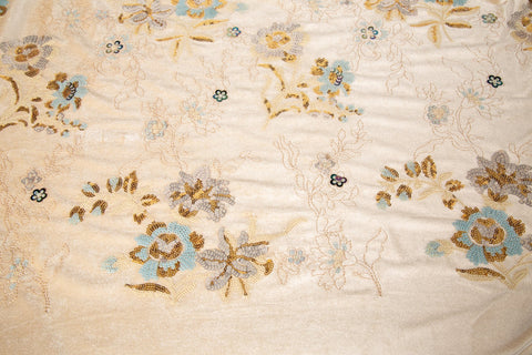 A sequin floral embroidery fabric on a cream velvet base, with blue and gold motifs.
