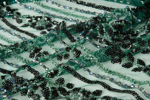 An emerald green Art Deco beaded fabric, with concentric, eye-shaped patterns in black sequins and beads.
