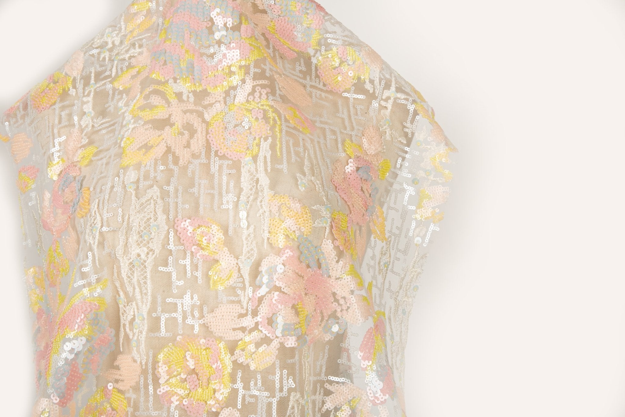 A sequin embroidery fabric on nude mesh with pastel florals over white geometric patterns.