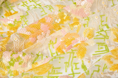 A sequin embroidery fabric on white mesh with yellow-pink florals over green geometric patterns.
