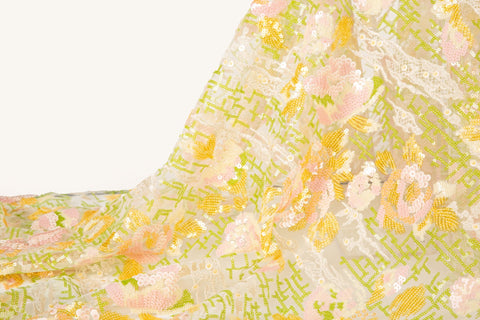 A sequin embroidery fabric on white mesh with yellow-pink florals over green geometric patterns.
