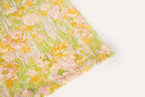 A sequin embroidery fabric on white mesh with yellow-pink florals over green geometric patterns.
