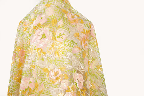 A sequin embroidery fabric on white mesh with yellow-pink florals over green geometric patterns.
