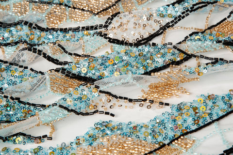 An Art Deco style geometric beaded fabric, with a mosaic or shattered pattern in gold, aqua, and black.
