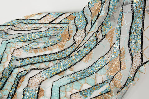 An Art Deco style geometric beaded fabric, with a mosaic or shattered pattern in gold, aqua, and black.
