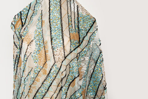 An Art Deco style geometric beaded fabric, with a mosaic or shattered pattern in gold, aqua, and black.
