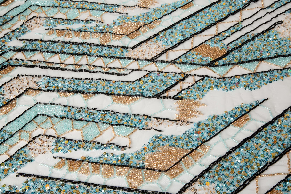 An Art Deco style geometric beaded fabric, with a mosaic or shattered pattern in gold, aqua, and black.
