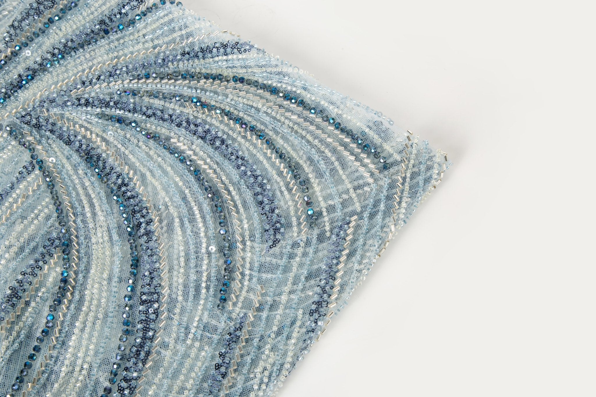 A blue and silver hand-beaded fabric, with an abstract, flowing pattern resembling water currents or mineral strata.
