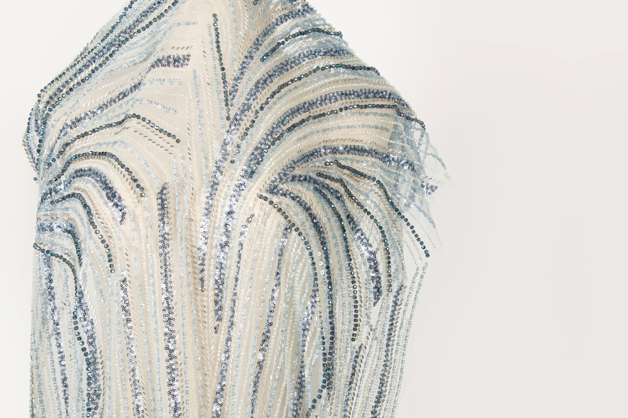 A blue and silver hand-beaded fabric, with an abstract, flowing pattern resembling water currents or mineral strata.
