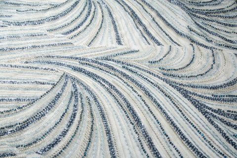 A blue and silver hand-beaded fabric, with an abstract, flowing pattern resembling water currents or mineral strata.
