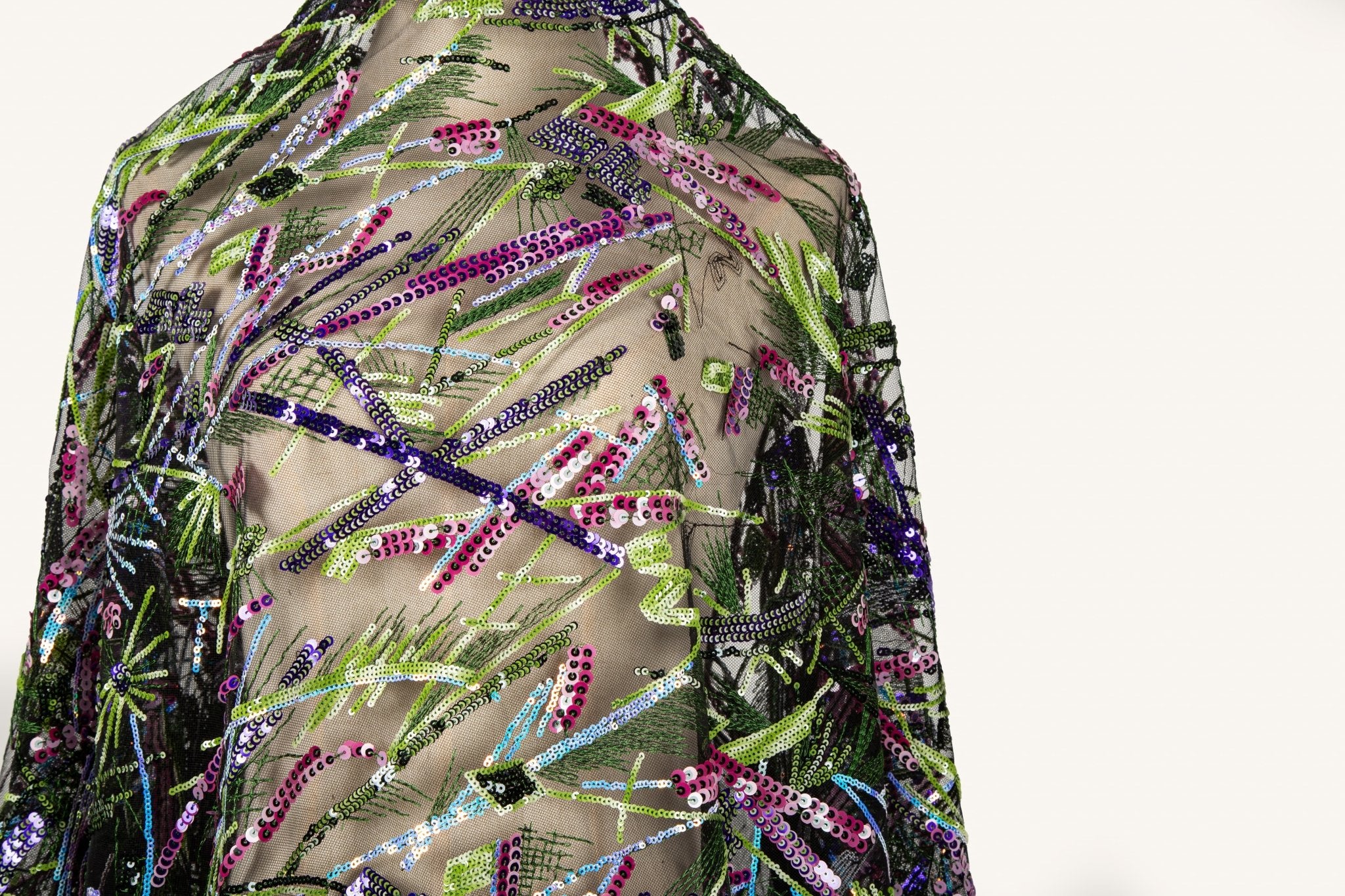  An abstract embroidery fabric on black tulle, with a graffiti-like pattern of lines made from neon green, pink, and purple sequins and thread