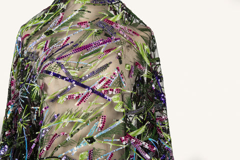  An abstract embroidery fabric on black tulle, with a graffiti-like pattern of lines made from neon green, pink, and purple sequins and thread